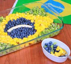 a bowl of fruit is sitting next to a plastic container with blueberries and mangos in it