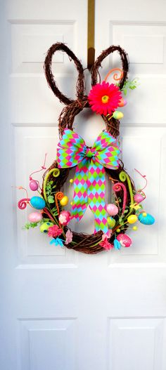 an easter wreath hanging on the front door with bunny ears and colorful eggs around it