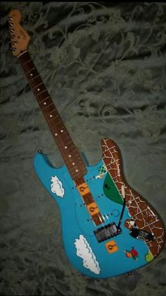 a blue guitar with giraffes painted on the body and neck, sitting on a bed