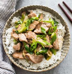 a bowl filled with rice and meat on top of a table next to chopsticks