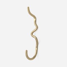 a gold hook that is hanging on the side of a white wall and has a curved handle