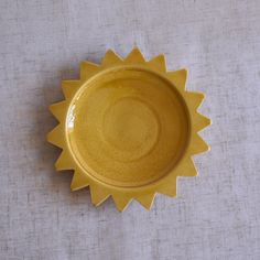 a yellow sun shaped bowl sitting on top of a white cloth covered tablecloth,