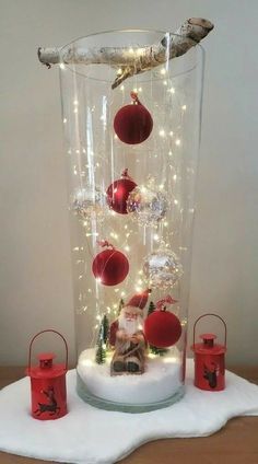 a glass vase filled with ornaments on top of a white cloth covered table next to two red candles