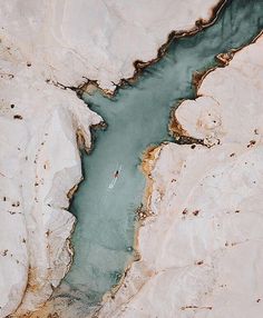 an aerial view of a body of water surrounded by white mountains and brown rocks, with a lone boat in the middle