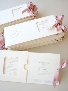 three folded wedding cards with pink bows on them, one in white and the other in gold