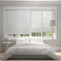 a bed with white sheets and pillows next to a window covered in blind shades that are open