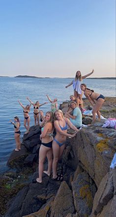 a group of women in bikinis standing on rocks near the water with their arms up