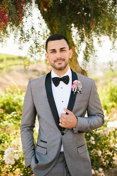 a man in a tuxedo and bow tie standing under a tree with flowers