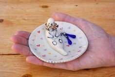 a hand holding a small white plate with scissors and a figurine on it