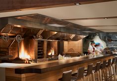 two chefs are preparing food in a restaurant kitchen with bar stools and wood paneled walls