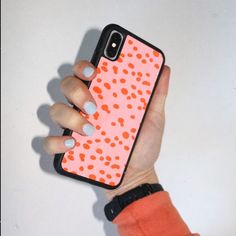 a woman's hand holding an orange and white polka dot phone case