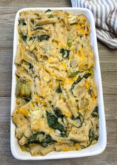 a casserole dish filled with pasta and spinach on a wooden table next to a striped towel