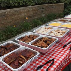 several trays of food are on a table outdoors with red and white checkered cloth