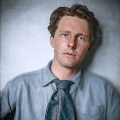 a man wearing a blue shirt and tie posing for a photo in front of a gray wall