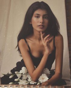 a woman sitting on the floor with flowers in front of her and holding her hand to her chin