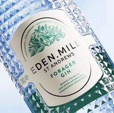 a bottle of eden mill forager gin on a blue background with green leaves