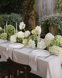 a long table with white flowers and candles on it is set for an outdoor dinner