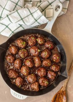 some meatballs are being cooked in a skillet with sauce on the side and a wooden spoon next to it