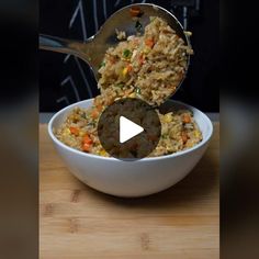 a bowl filled with rice and vegetables on top of a wooden table