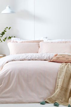 a bed with pink and white striped comforter next to a plant on a table