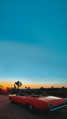 an old red car parked in the desert at sunset