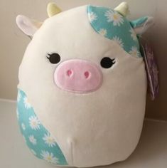 a stuffed cow with flowers on it's head is sitting next to a wall