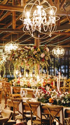 a dining room filled with lots of tables covered in flowers and chandelier hanging from the ceiling