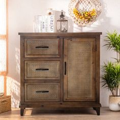 a wooden cabinet with three drawers next to a potted plant and wicker basket