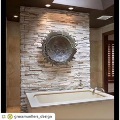 a bath tub sitting in front of a stone wall with a circular mirror above it