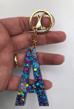 a hand holding a keychain shaped like the letter a with multicolored sprinkles