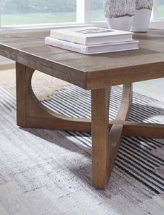 a coffee table with two books on top and a vase next to it in front of a window