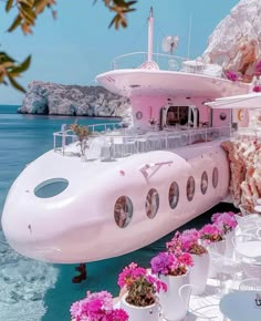 a large white boat sitting on top of the ocean next to a cliff covered in pink flowers