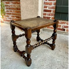 an old wooden stool with roped legs and seat cushion on the ground in front of a brick wall