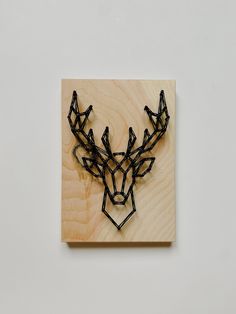 a deer head made out of black string on a wooden block with white wall in the background