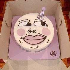 a birthday cake in a box with a face drawn on the side and a party hat on top