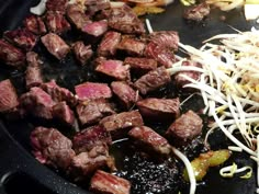 steak and onions being cooked in a skillet with grated cheese on the side