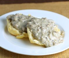 two biscuits covered in gravy on a white plate with a brown table cloth