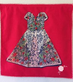 a red and blue dress with flowers on it is hanging on the wall in front of a white wall