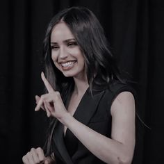 a woman is smiling and making the peace sign with her hands while standing in front of a black background