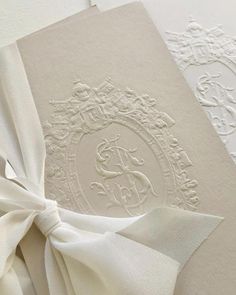 a white wedding card with a bow on the front and back, decorated with an ornate monogram