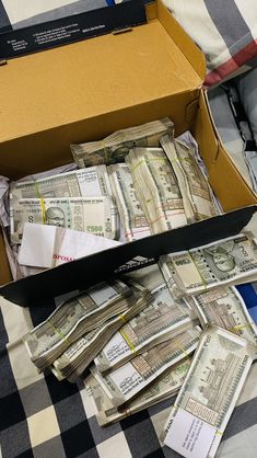 an open box filled with money sitting on top of a checkered cloth covered bed