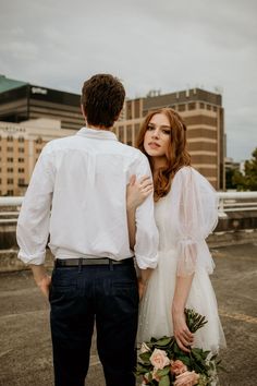 a man and woman standing next to each other in front of tall buildings with their arms around each other