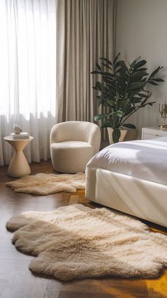 a white bed sitting in a bedroom next to two chairs and a table with a potted plant on top of it