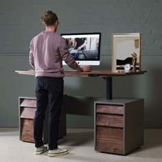 a man standing in front of a desk with a computer monitor on top of it