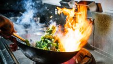 a wok filled with food cooking on top of a stove next to a fire