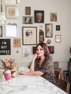 a woman sitting at a table in front of pictures on the wall