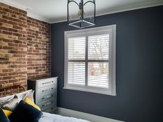 a bedroom with a brick wall and white shutters on the windowsill is shown