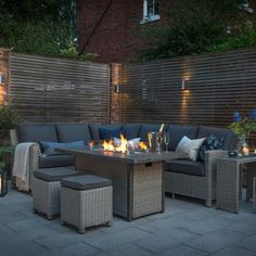 an outdoor fire pit surrounded by patio furniture and candles in the evening time with lights on