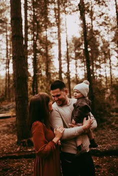 a man and woman are holding their son in the woods while he holds his baby