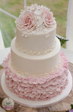 a three tiered cake with pink flowers and pearls on the top is sitting on a table